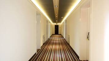 Un pasillo de hotel con alfombra a rayas, paredes blancas e iluminación empotrada en el techo.