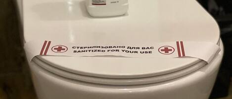 A white toilet with a bottle of hand sanitizer on top.