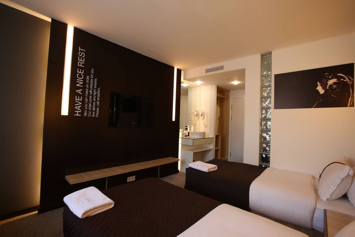 Hotelkamer met twee bedden, een bankje, een spiegel, een televisie en een muur met een bericht.