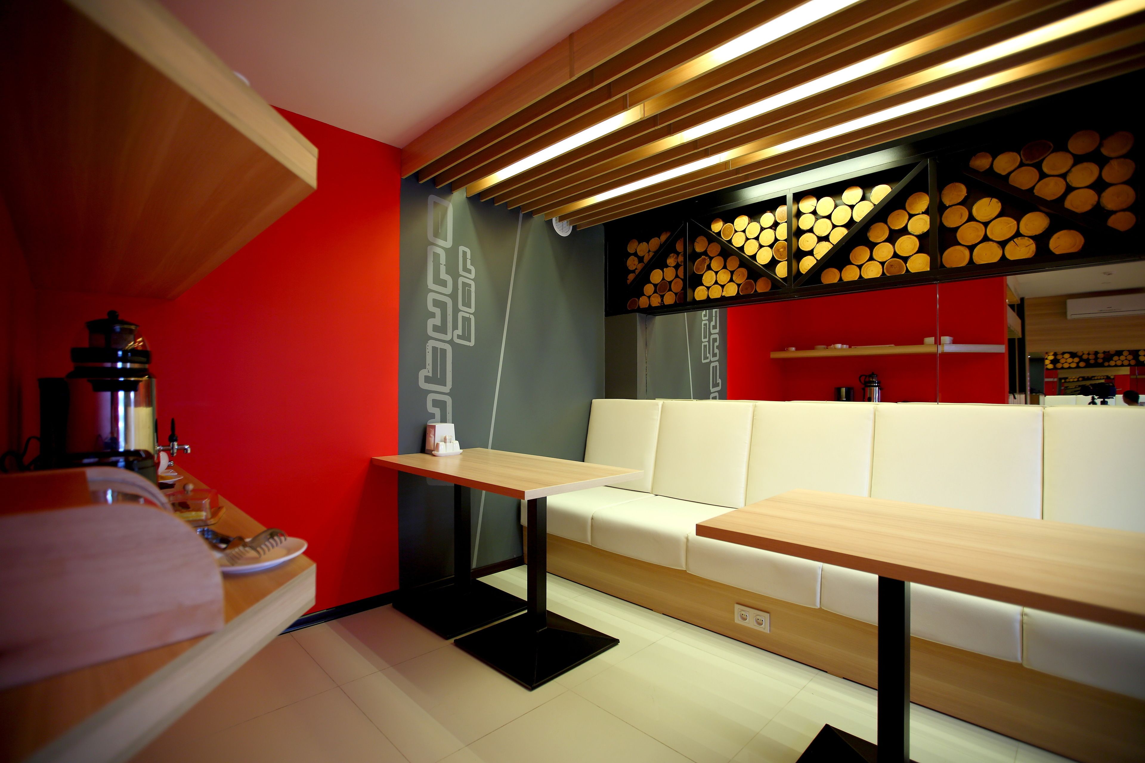 A modern kitchen with a red accent wall, white seating, and a wooden ceiling.