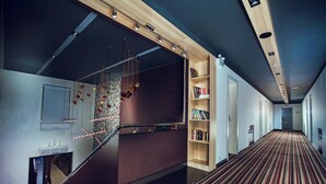 A modern hotel lobby with a staircase, a bookshelf, and a patterned carpet.