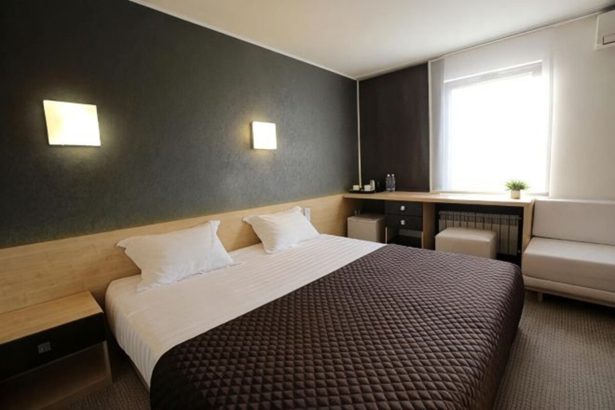 Een hotelkamer met een bed, nachtkastjes, een bureau, een stoel en een raam.