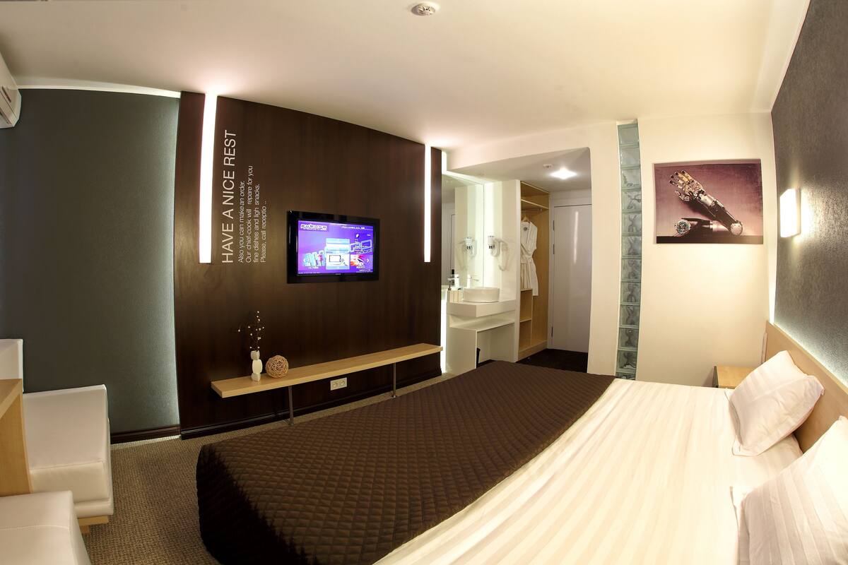Een moderne hotelkamer met een groot bed, een aan de muur bevestigde televisie, een kaptafel met spiegel en een lijst met een foto.