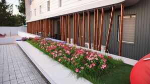 A modern building with a long, narrow garden with pink flowers and wooden slats.