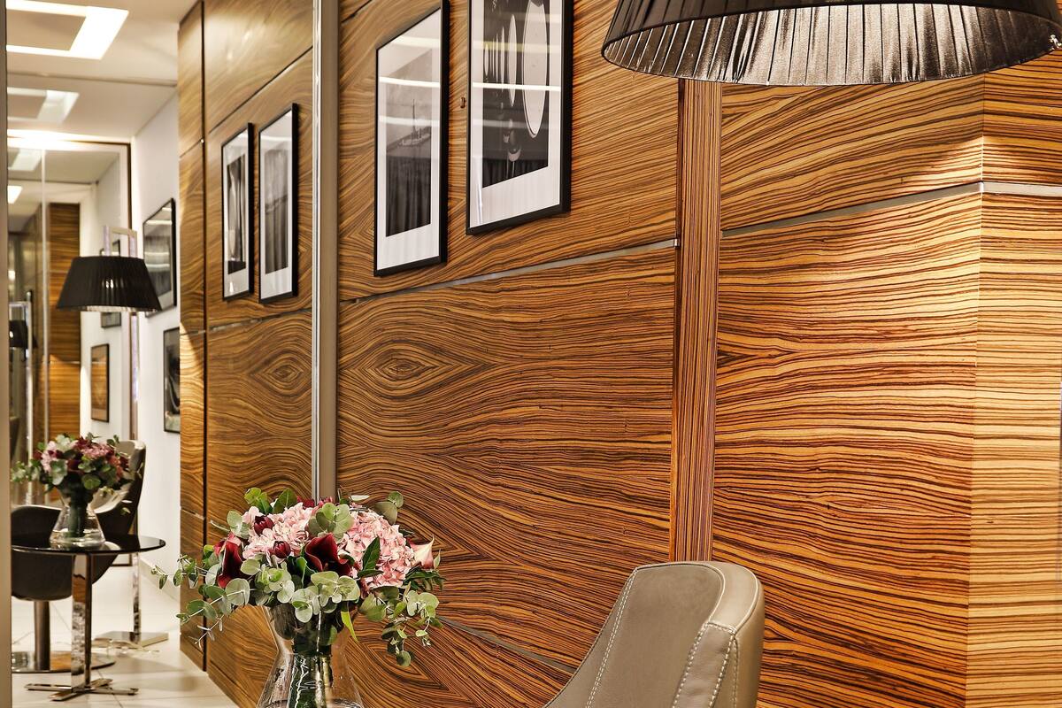 A modern interior with a leather chair, wooden panel wall, framed pictures, and a vase with flowers.