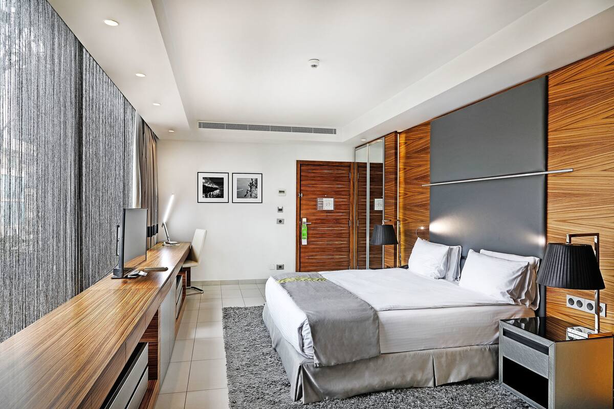 A modern bedroom with a large bed, a desk, and a wardrobe.
