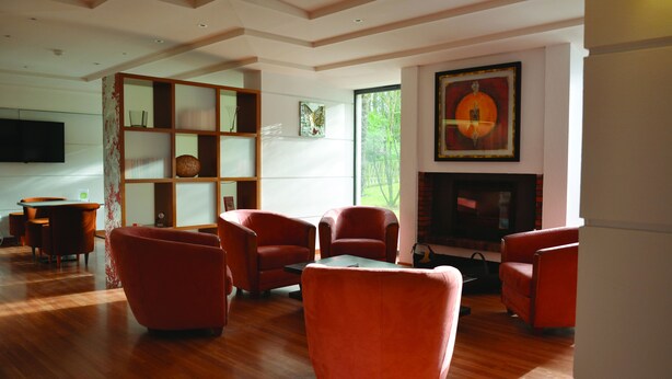 A modern living room with wooden flooring, red armchairs, a glass coffee table, and a fireplace. - Contact Hotel du Parc (Orvault)