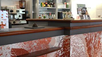 Zona de bar con una máquina de café, estanterías con botellas y vasos, y un atril para el menú.