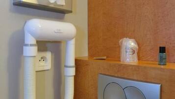 A hotel room with a hand dryer, a tissue box, and a small shelf with toiletries.