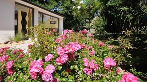 A modern building with a glass facade, surrounded by a garden with pink roses. - Contact Hotel du Parc (Orvault)