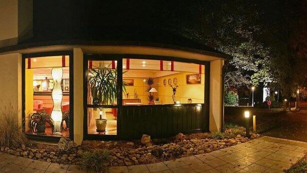 A small, well-lit building with a reception area, surrounded by a landscaped garden with rocks and plants. - Contact Hotel du Parc (Orvault)
