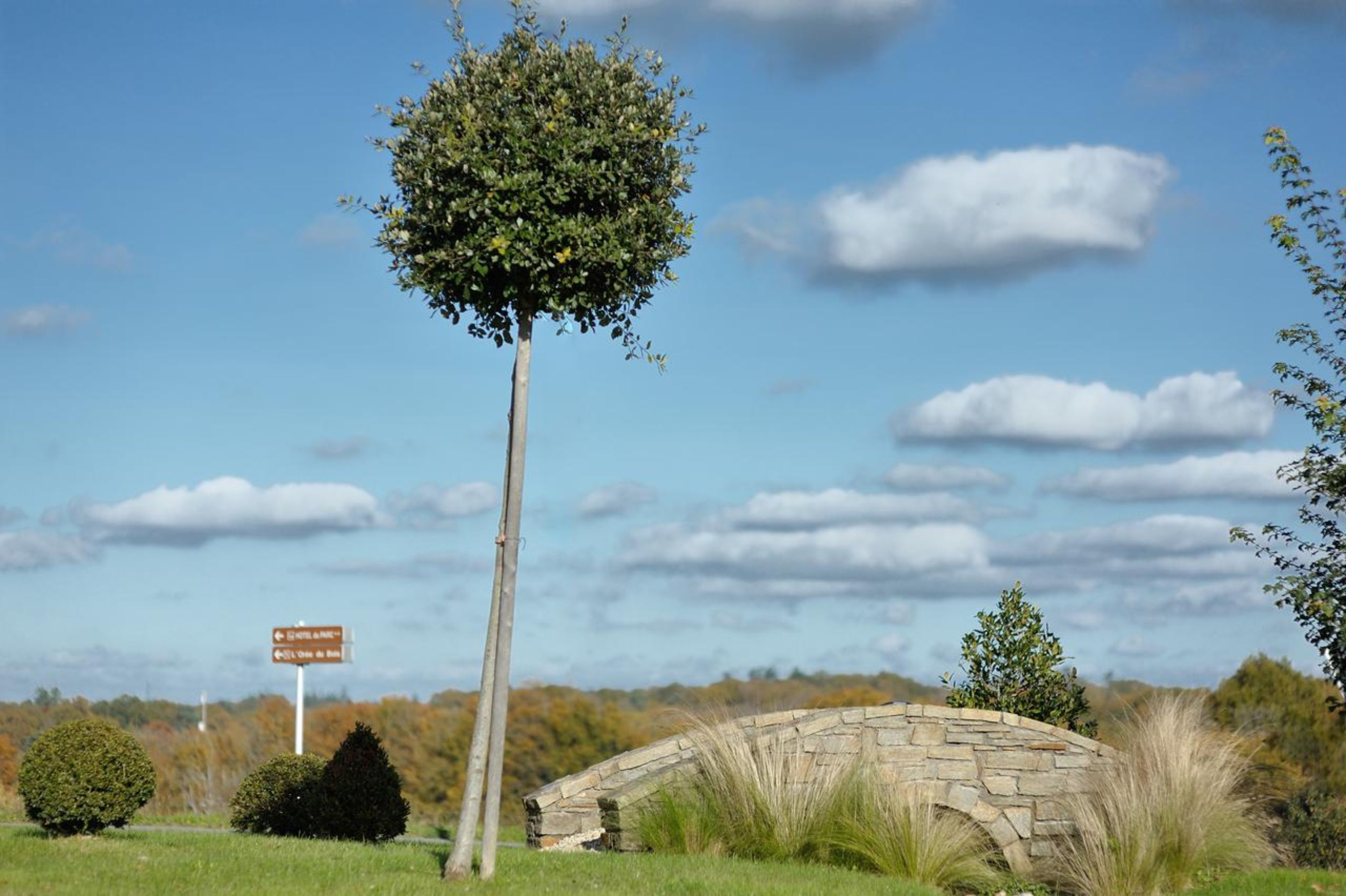 Un pont de pierre, un panneau indicateur et un arbre, le tout dans un cadre rural.