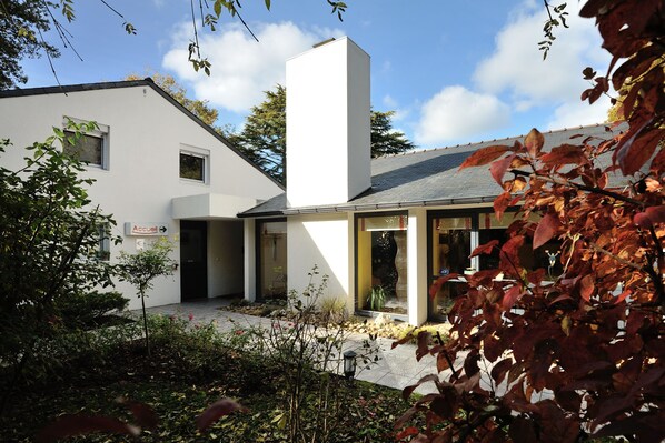 A modern building with a white facade, a chimney, and a small garden area with plants and a pathway. - Contact Hotel du Parc (Orvault)