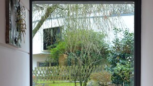 A view through a glass door into a garden with a small tree, a wooden bench, and a white fence. - Contact Hotel du Parc (Orvault)