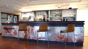 A bar area with a wooden counter, two bar stools, and a wall with a red abstract design. - Contact Hotel du Parc (Orvault)