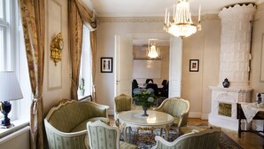 A room with a round table, four chairs, a chandelier, a fireplace, and a view into another room.
