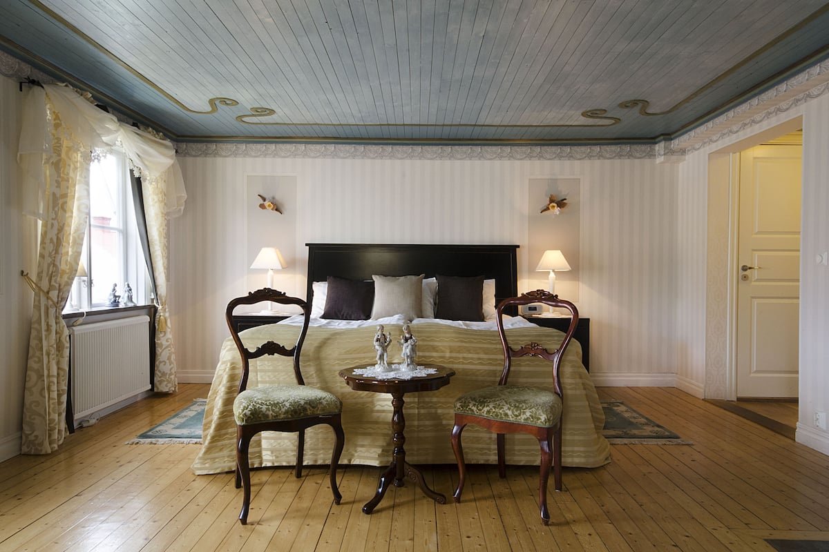 Un dormitorio con una cama grande, dos sillas, una mesita y un radiador.