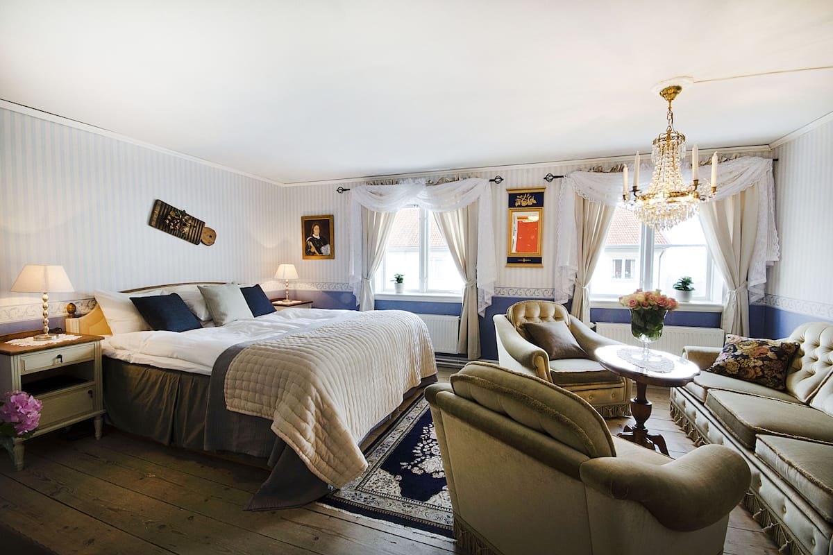 Un dormitorio elegante con una cama grande, un área de descanso con una mesa y sillas, y un candelabro.