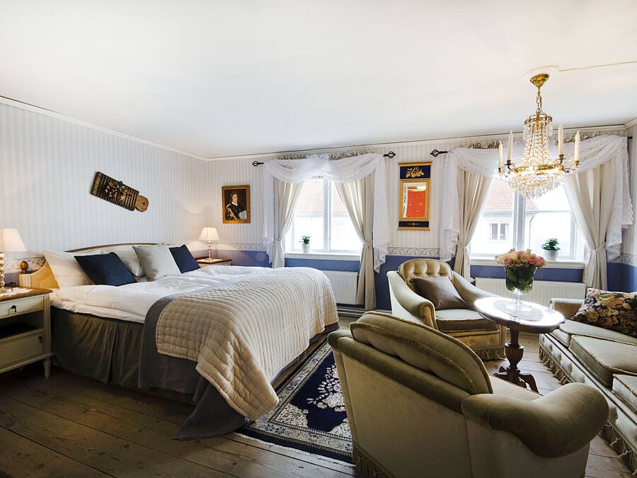 A well-appointed bedroom with a large bed, a sitting area with a table and chairs, and a chandelier.