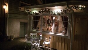 A covered outdoor seating area with a table and chairs, decorated with lights and garlands.
