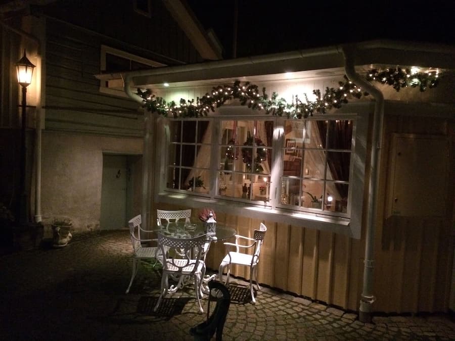 A covered outdoor seating area with a table and chairs, decorated with lights and garlands.