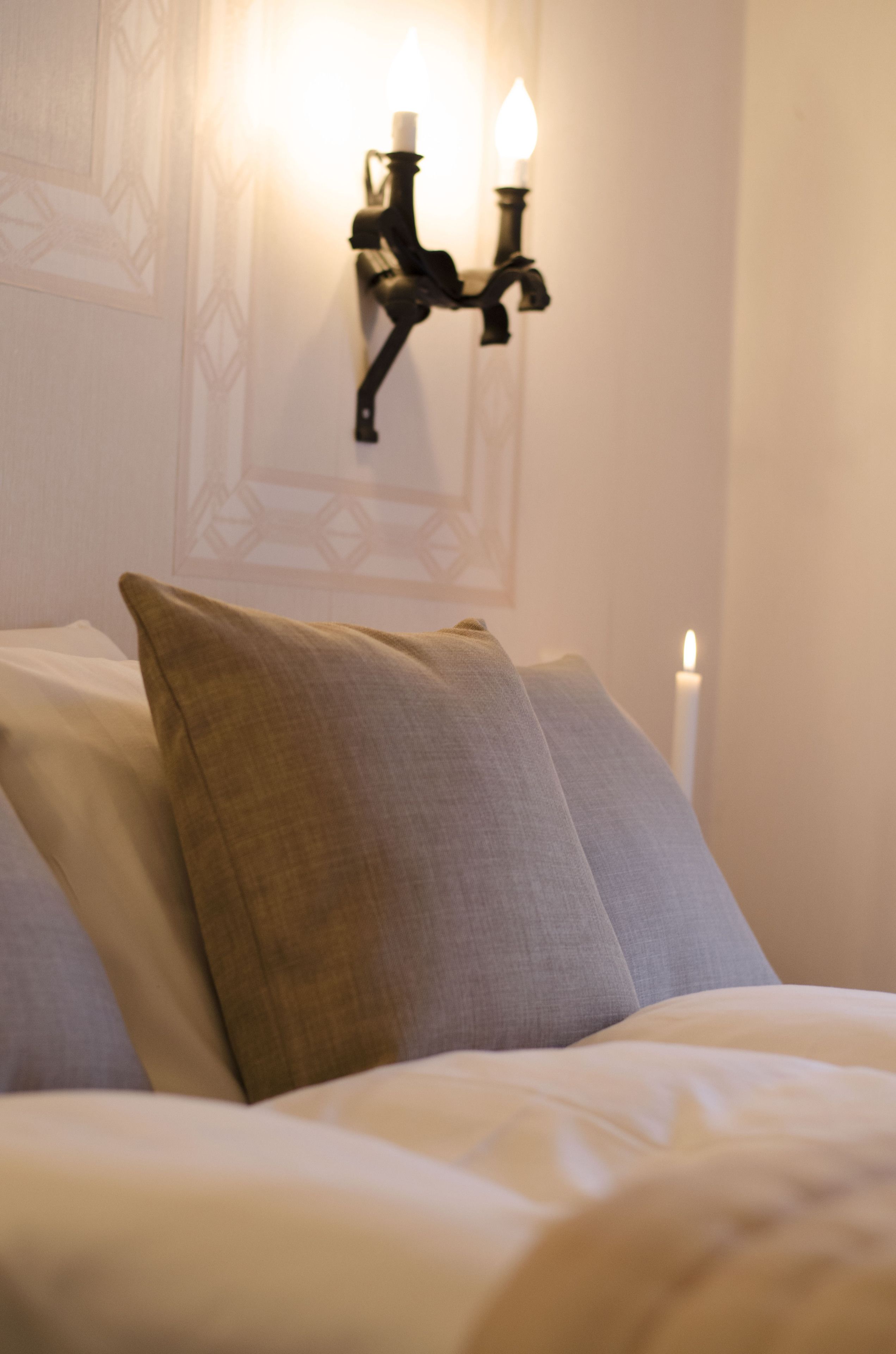 Una cama con almohadas y una lámpara fijada a la pared.