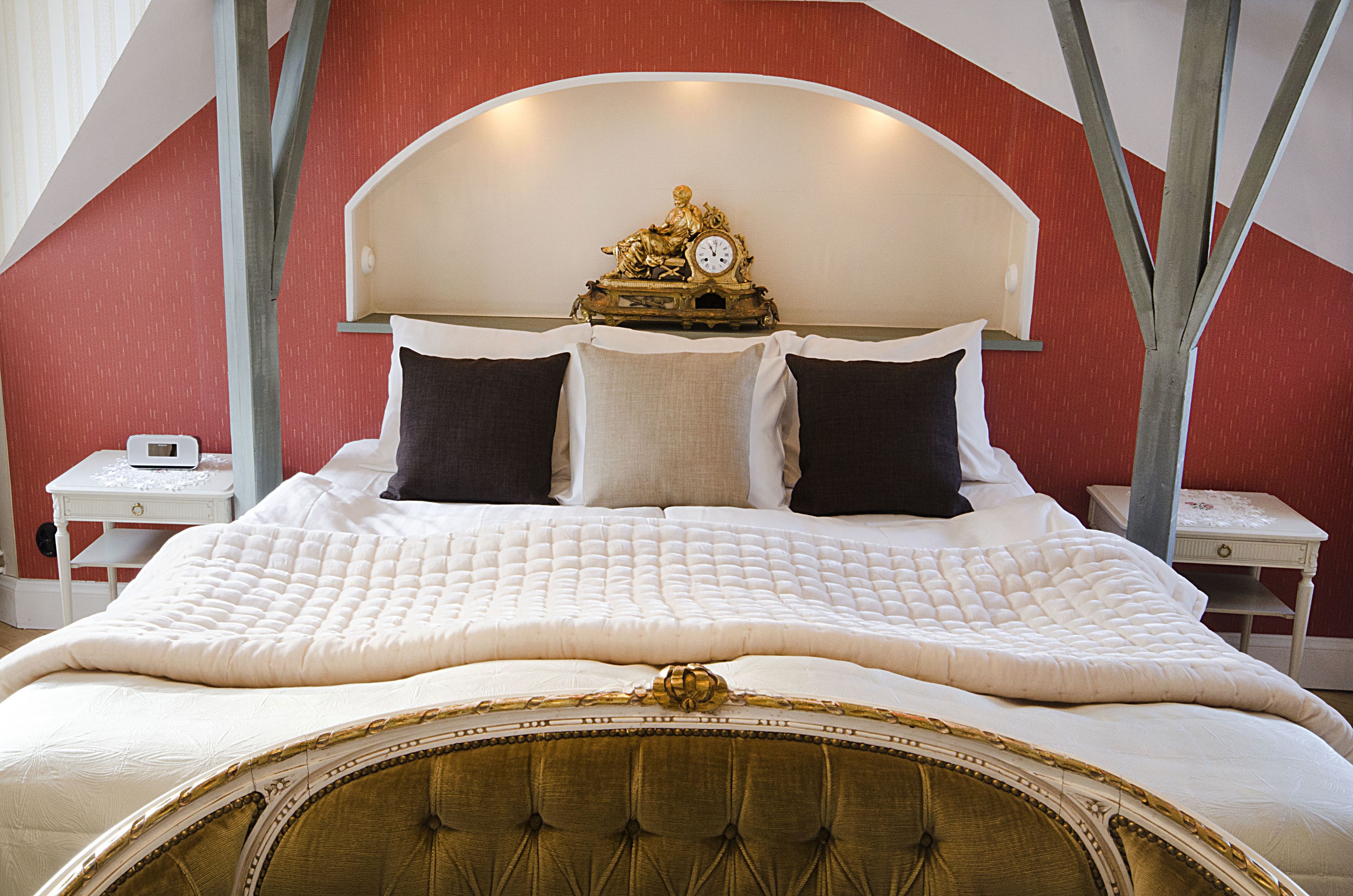 A large bed with a white quilted bedspread, a tufted headboard, and a decorative clock above it. There are two bedside tables with lamps.
