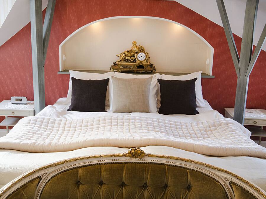 A large bed with a white quilted bedspread, a tufted headboard, and a decorative clock above it. There are two bedside tables with lamps.