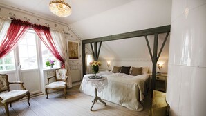 A bedroom with a bed, a chair, a table, and a window with curtains.