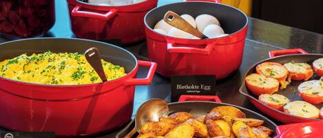 A buffet with various dishes including scrambled eggs, roasted potatoes, and eggs in red pots.
