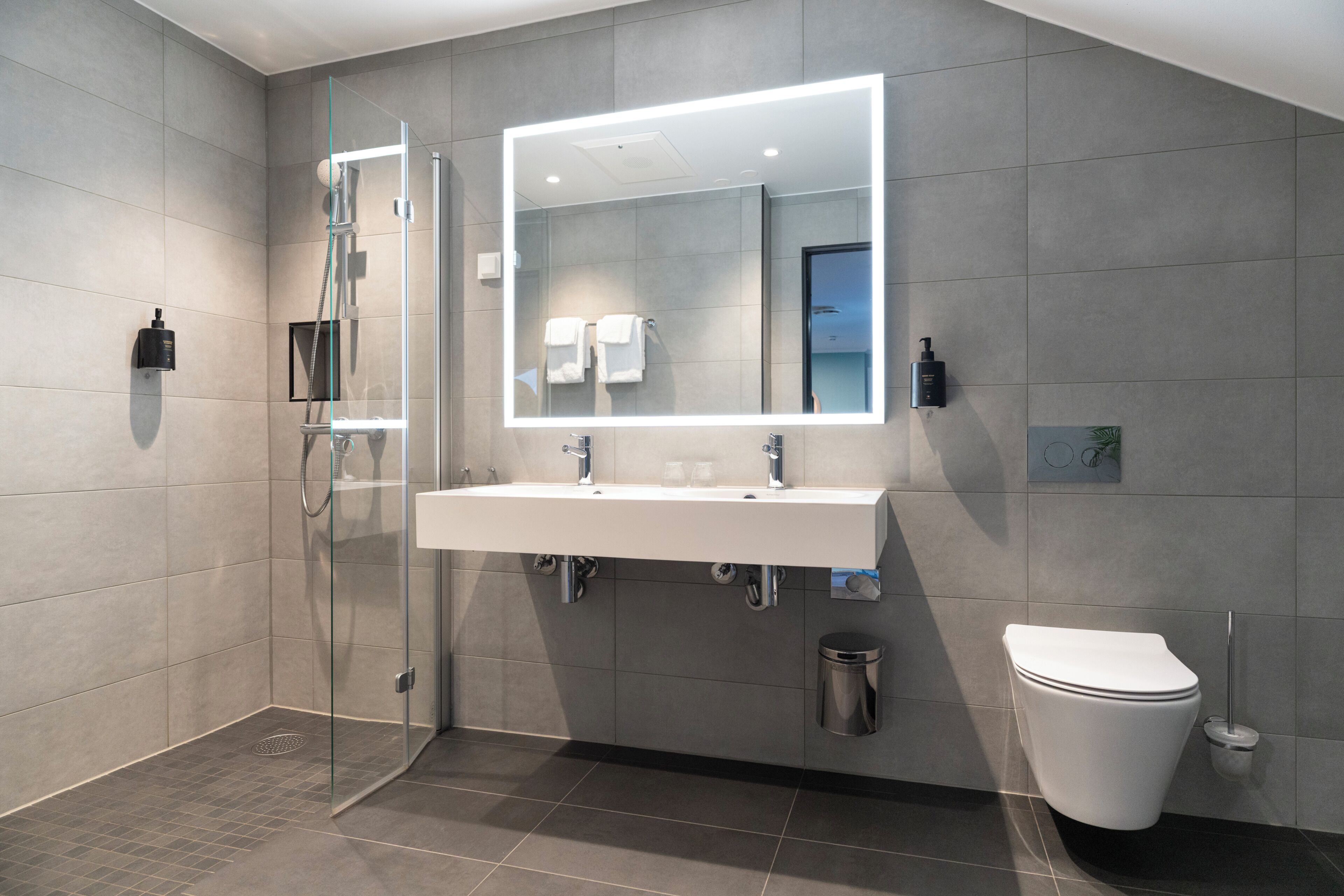 A modern bathroom with a glass-enclosed shower, a large mirror, a white sink, and a toilet.