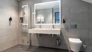 A modern bathroom with a glass-enclosed shower, a large mirror, a white sink, and a toilet.