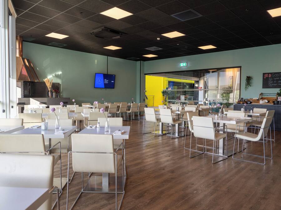 A spacious dining area with multiple tables and chairs, a television screen on the wall, and a visible exit sign.