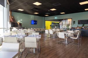 A spacious dining area with multiple tables and chairs, a television screen on the wall, and a visible exit sign.