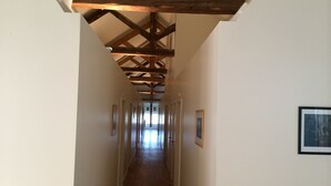 Un pasillo largo y estrecho con vigas de madera en el techo y cuadros enmarcados en las paredes.