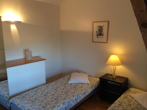 Two single beds with floral-patterned bedding and a wall-mounted shelf are featured in this cozy room.