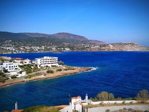 Une ville côtière avec des bâtiments qui bordent le littoral, une mer d’un bleu limpide et des collines en arrière-plan.