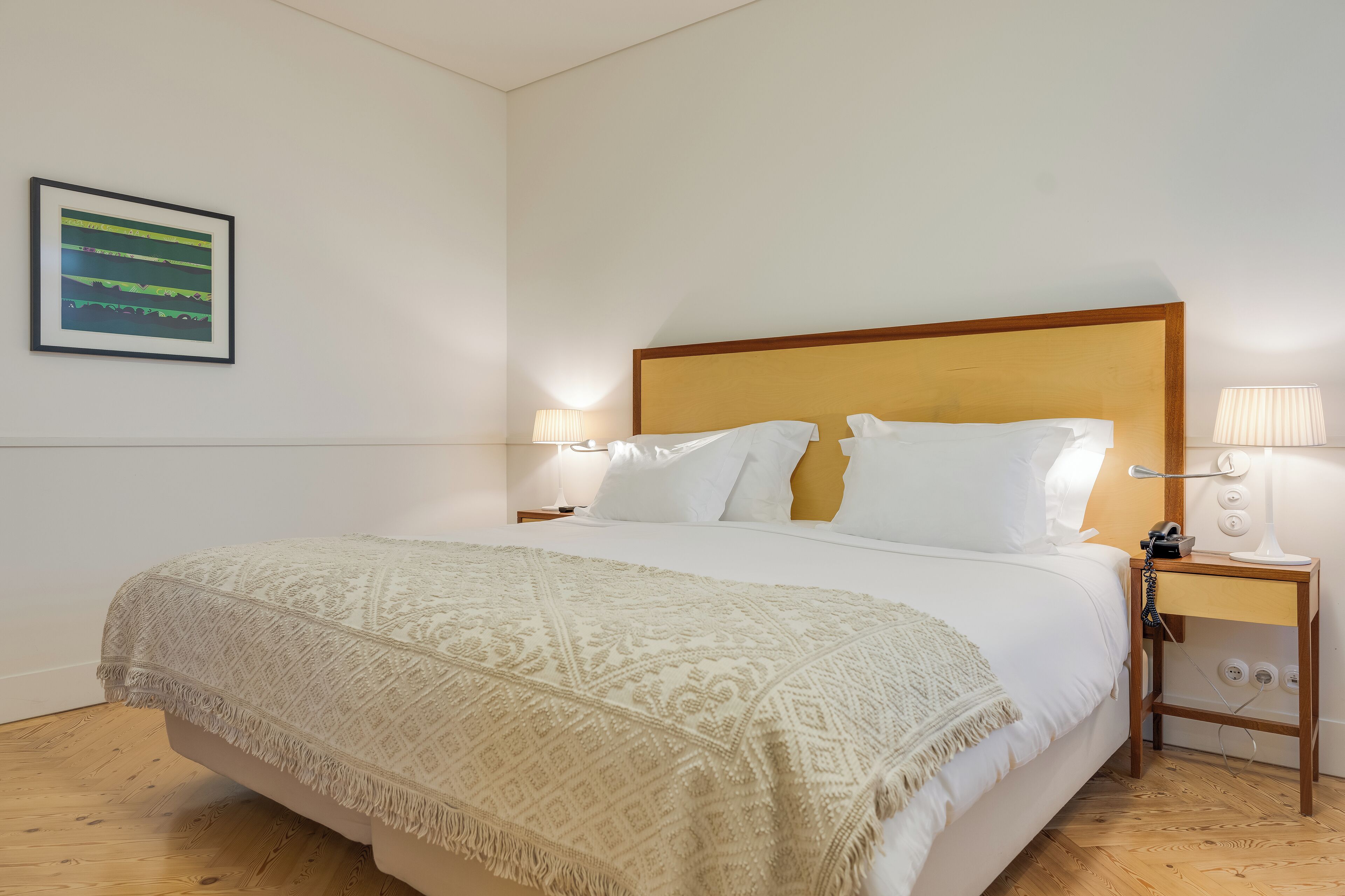 Una cama bien tendida con una colcha estampada, un cabecero de madera y lámparas de noche.