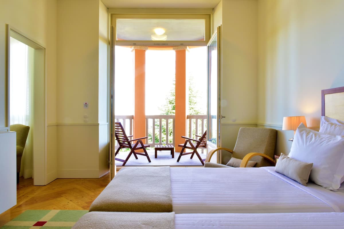 Een hotelkamer met een bed, een stoel, een klein tafeltje en een balkon met stoelen.