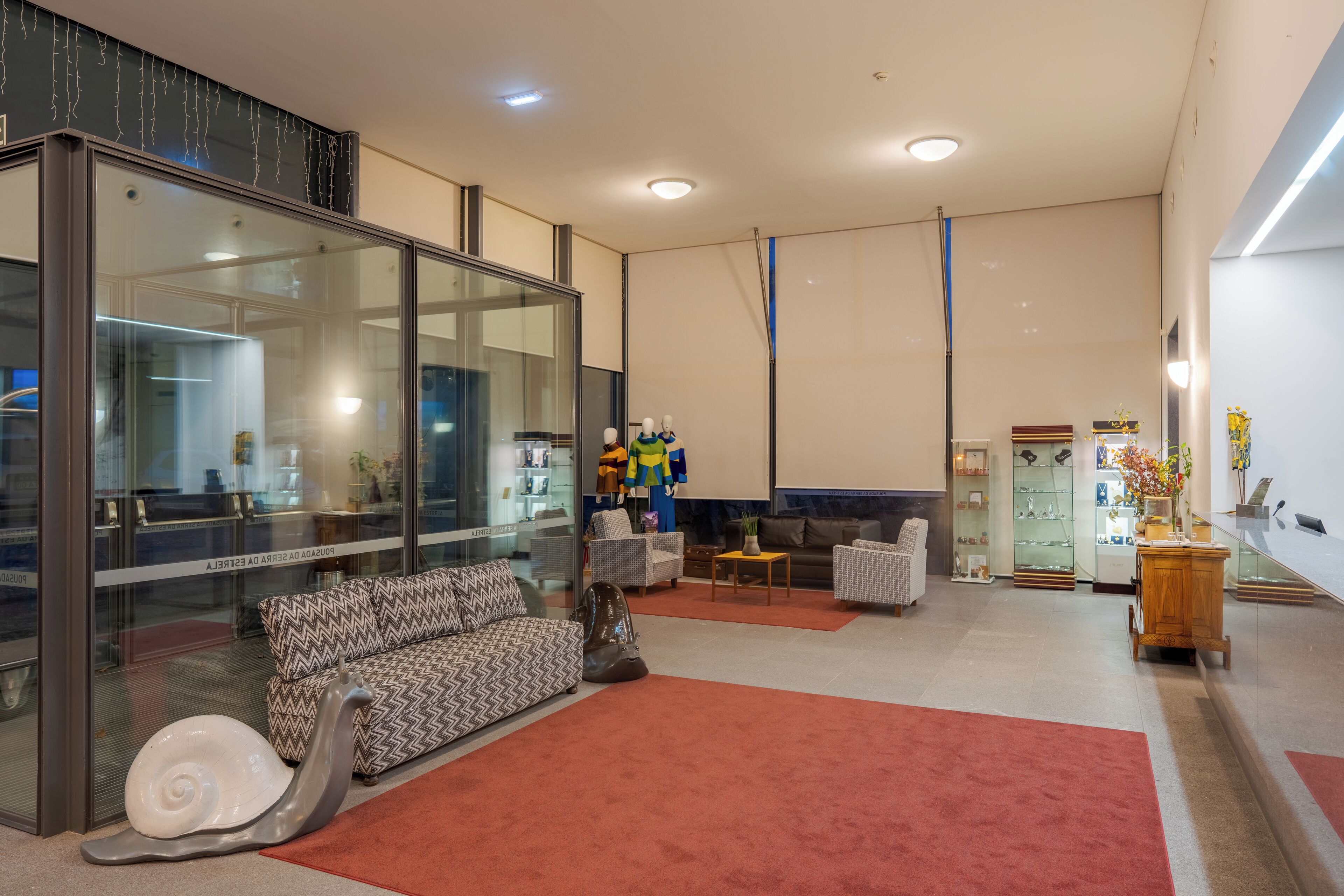 Una sala de estar moderna con un separador de vidrio, un sofá estampado, una alfombra roja y una exhibición de ropa colorida.