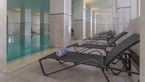 Une rangée de chaises longues avec des serviettes, une piscine à débordement et des colonnes en marbre.