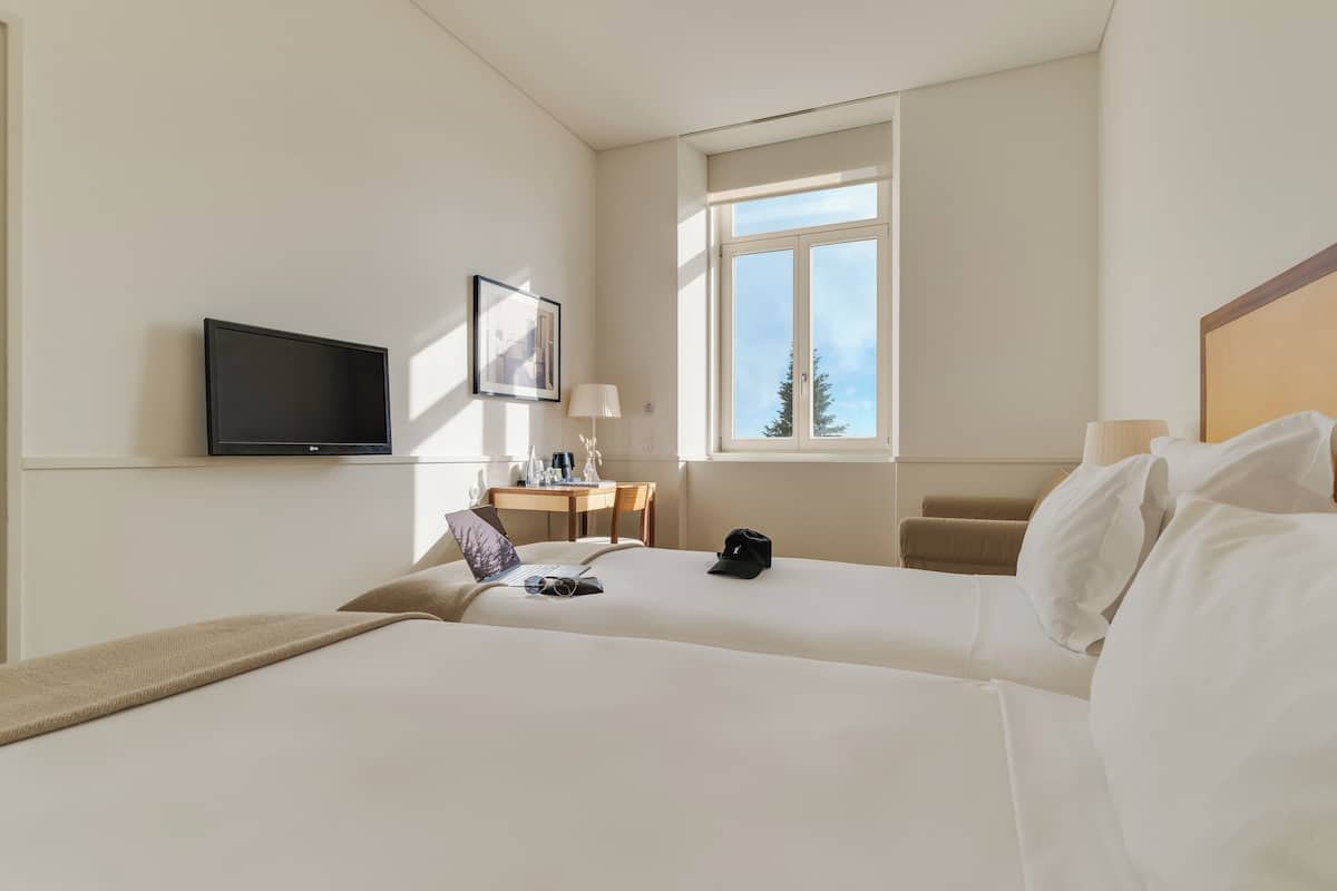 Hotelkamer met twee bedden, een bureau met stoel, een televisie, een raam en een lamp.