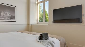 Habitación de hotel con una cama, un cuadro enmarcado en la pared, una ventana con vista a árboles y un televisor de pantalla plana montado en la pared.
