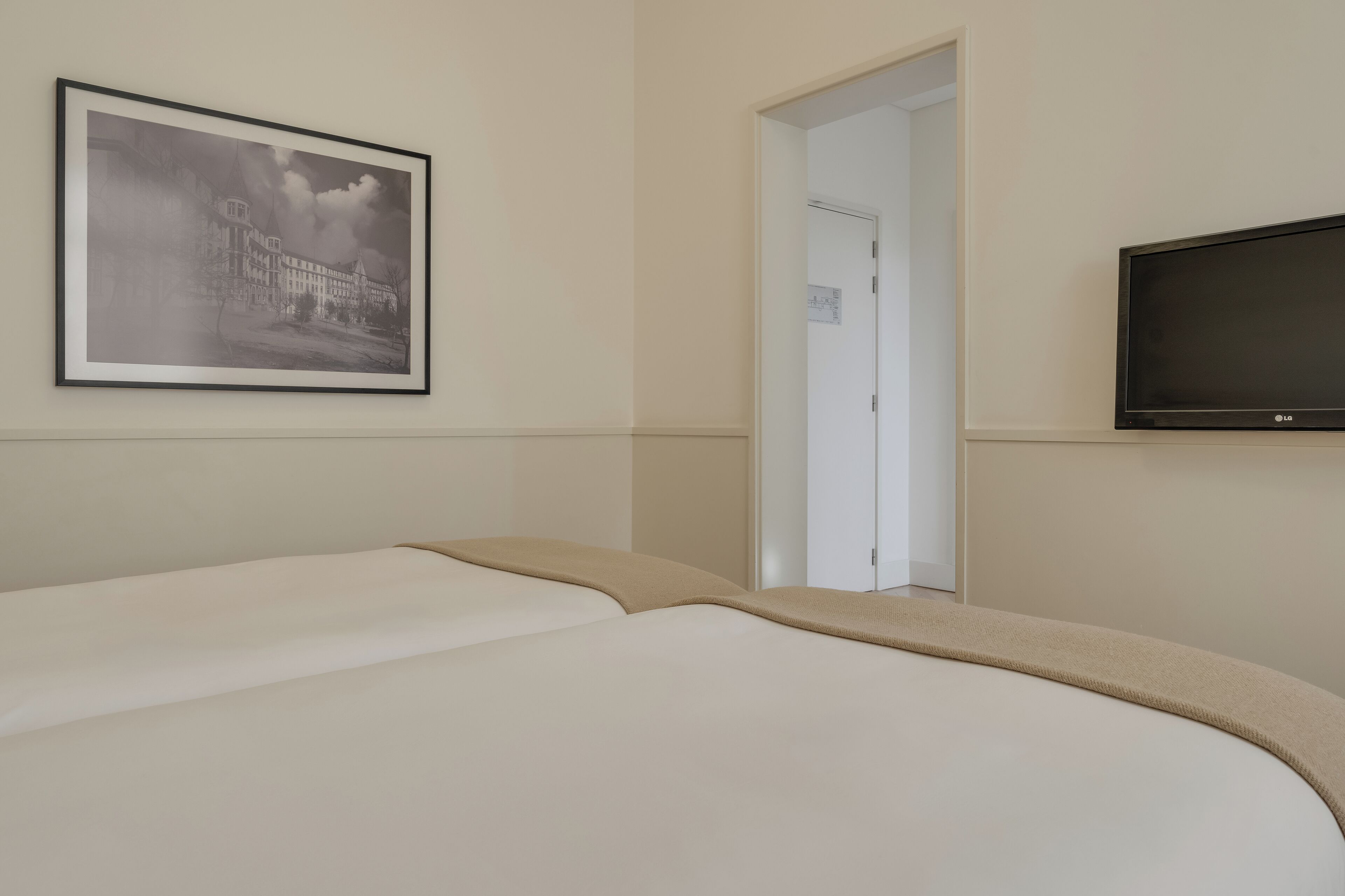 A hotel room with a bed, a framed picture on the wall, a television, and a door leading to another room.