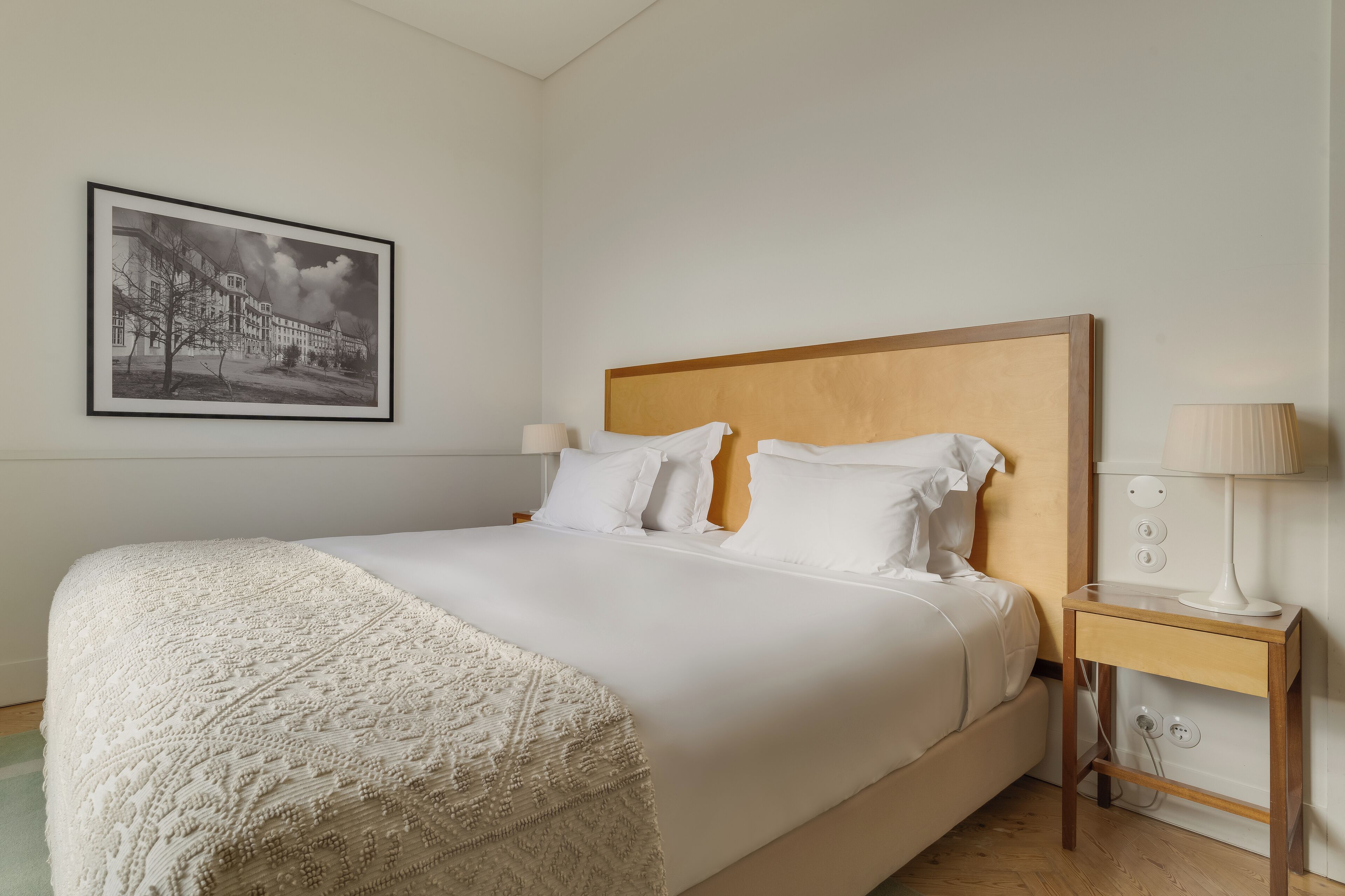 A neatly made bed with a wooden headboard, a bedside table with a lamp, and a framed picture on the wall.