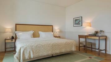 Une chambre bien rangée, avec un grand lit, des lampes de chevet, un bureau avec une chaise et un tableau encadré au mur.
