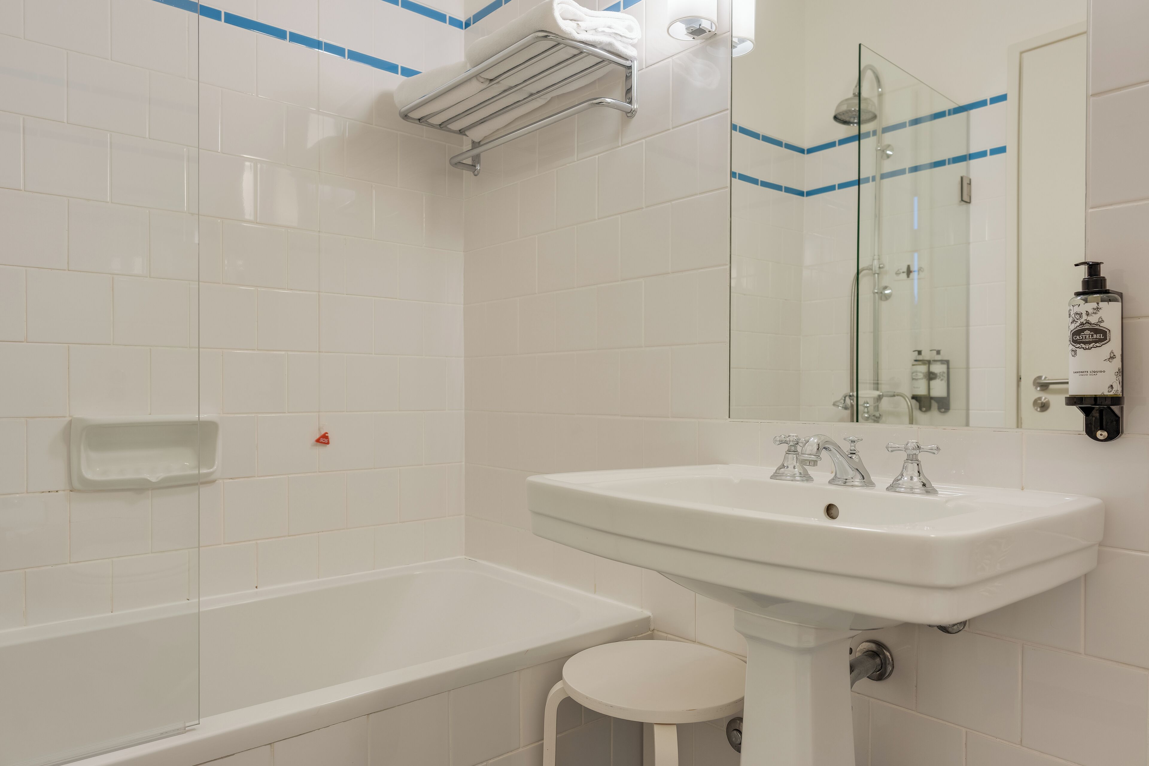 Une salle de bain avec un lavabo blanc, une cabine de douche en verre et un petit tabouret blanc.