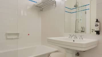 Une salle de bain avec un lavabo blanc, une cabine de douche en verre et un petit tabouret blanc.