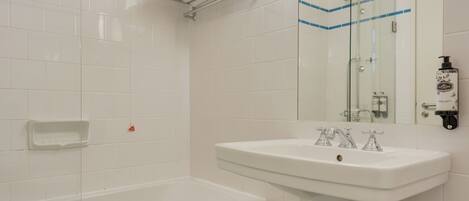 A bathroom with a white sink, a glass shower enclosure, and a small white stool.