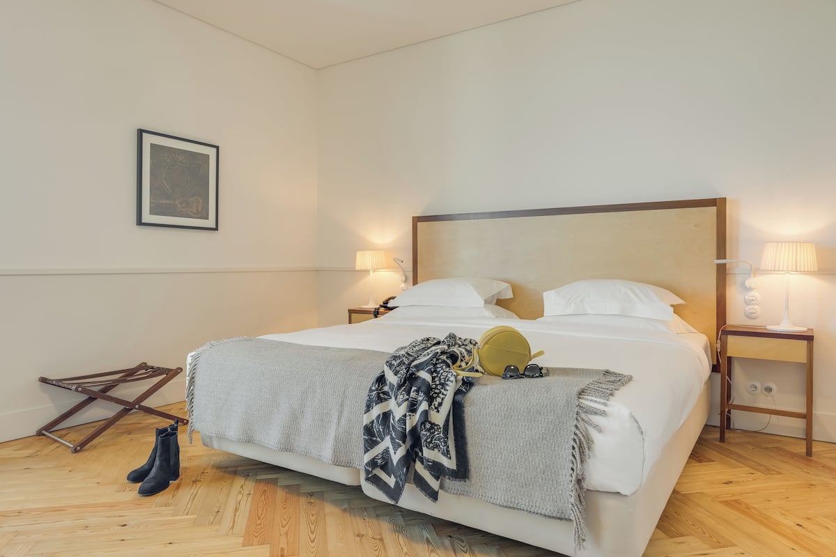 Een net opgemaakt bed met een geborduurde plaid, een paar laarzen en een klein tafeltje met een lamp ernaast.